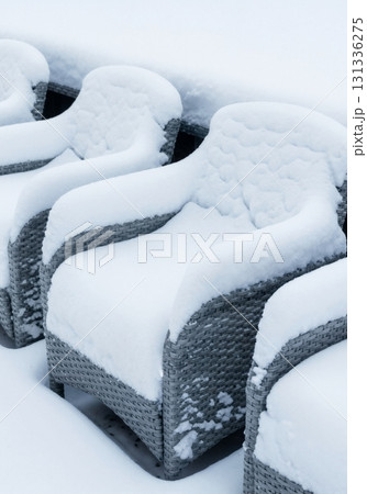 A row of grey woven patio chairs covered in a thick blanket of fresh snow. Outdoor furniture in cold winter weather. Off-season concept A row of grey woven patio chairs covered in a thick blanket of fresh snow. Outdoor furniture in cold winter weather. Off-season concept 131336275