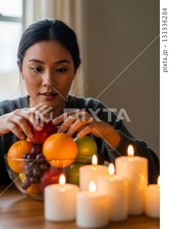 Young Asian woman arranging a fruit bowl by candlelight. Cozy home atmosphere for wellness and relaxation. Healthy lifestyle and self-care concept 131336284