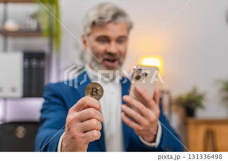 Middle-aged businessman checks crypto app on smartphone sees bitcoin rally gestures excited investor 131336498