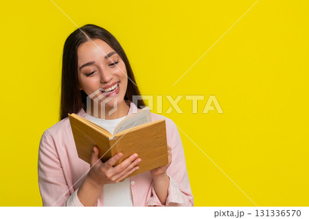 Young woman reading book with wide open eyes amazed expression intrigued thrilling surprising plot Young woman reading book with wide open eyes amazed expression intrigued thrilling surprising plot 131336570
