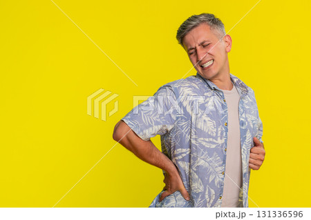 Adult man holding lower back straightening up with painful expression from strain or pinched nerve Adult man holding lower back straightening up with painful expression from strain or pinched nerve 131336596