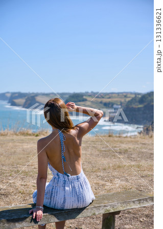 Young woman sitting on bench looking at ocean coast Young woman sitting on bench looking at ocean coast 131336621