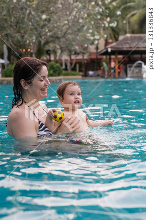 Caucasian woman holds son while swimming in pool on vacation.  131336843