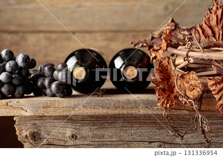 Bottles of red wine with grapes and dried vine on an old wooden table. 131336954