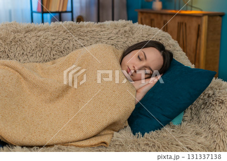Woman falling asleep tired after exhausting day wrapped in blanket laying head on pillow on sofa 131337138
