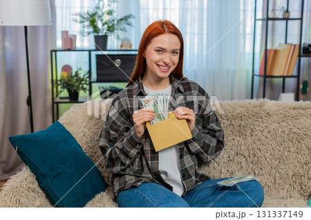 Woman sitting on sofa counting cash dollars putting part into envelope looking happy and satisfied Woman sitting on sofa counting cash dollars putting part into envelope looking happy and satisfied 131337149