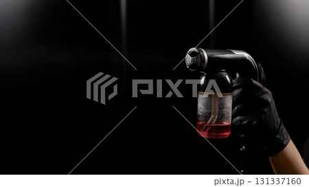 Close-up of instant tanning equipment in the hands of a master. Gun spraying paint for leather against black background Close-up of instant tanning equipment in the hands of a master. Gun spraying paint for leather against black background 131337160