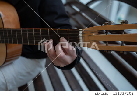 Caucasian man playing guitar while sitting on a bench.  131337202
