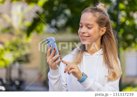 Happy Caucasian woman using smartphone typing text messages browsing internet on city town street Happy Caucasian woman using smartphone typing text messages browsing internet on city town street 131337239
