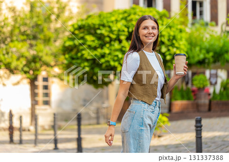 Happy Caucasian young pretty woman enjoying morning coffee hot drink and walking on city street Happy Caucasian young pretty woman enjoying morning coffee hot drink and walking on city street 131337388
