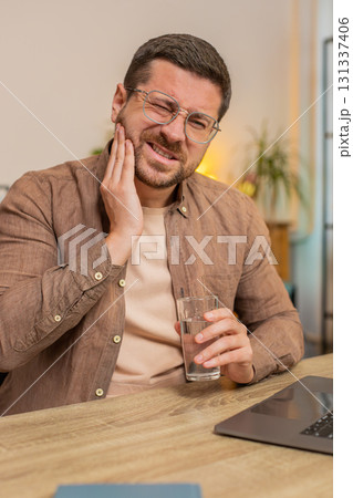 Man freelancer sitting at home office drinking cold water feeling toothache touching mouth at home Man freelancer sitting at home office drinking cold water feeling toothache touching mouth at home 131337406