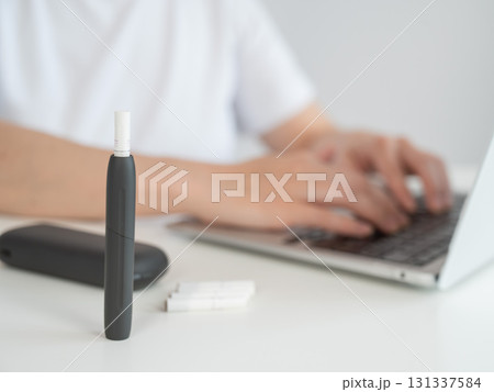 A woman smokes an electronic cigarette while working on a laptop. Tobacco heating system. A woman smokes an electronic cigarette while working on a laptop. Tobacco heating system. 131337584