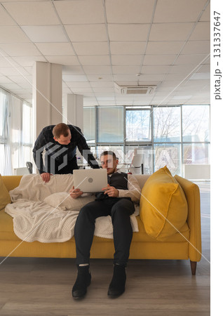 Two Caucasian men discussing work on a laptop while sitting on a sofa. Modern office.  131337647