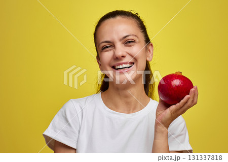 Beautiful smiling woman holding pomegranate on yellow background Beautiful smiling woman holding pomegranate on yellow background 131337818