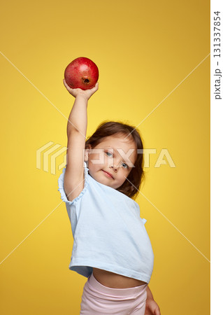 cute little child girl holding a pomegranate on yellow background. 131337854
