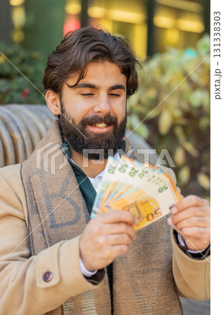 Successful rich happy young Indian man holding euro bill money cash fan on downtown city street Successful rich happy young Indian man holding euro bill money cash fan on downtown city street 131338303