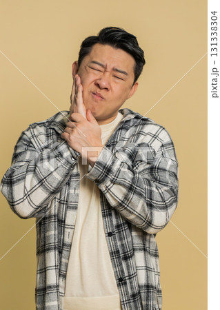 Asian man touching cheek closing eyes with expression of terrible suffer from painful toothache Asian man touching cheek closing eyes with expression of terrible suffer from painful toothache 131338304