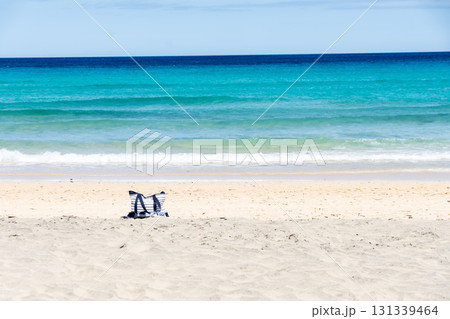 深い青とエメラルドグリーンの海岸の白い砂浜に置かれたバッグ　カナリア諸島のフエルテベンテュラ島にて 131339464