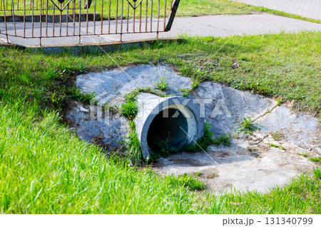 A large concrete pipe is resting on the grass right next to a sidewalk 131340799