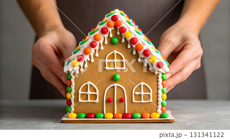 Hands assembling a colorful gingerbread house during holiday celebrations in a cozy kitchen Hands assembling a colorful gingerbread house during holiday celebrations in a cozy kitchen 131341122
