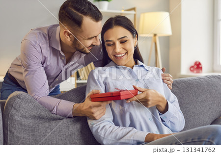 Young woman holding red present gift box in hand from her boyfriend sitting on sofa at home Young woman holding red present gift box in hand from her boyfriend sitting on sofa at home 131341762