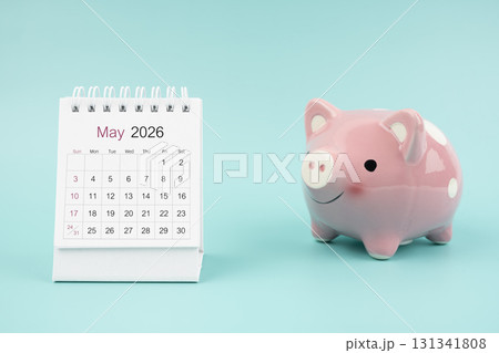 May 2026 Desk calendar and pink piggy bank on blue background. 131341808