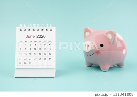 June 2026 Desk calendar and pink piggy bank on blue background. 131341809