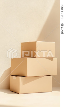 Three closed cardboard boxes of different sizes are stacked on top of each other, creating a balanced composition against a beige backdrop with contrasting light and shadow 131343885