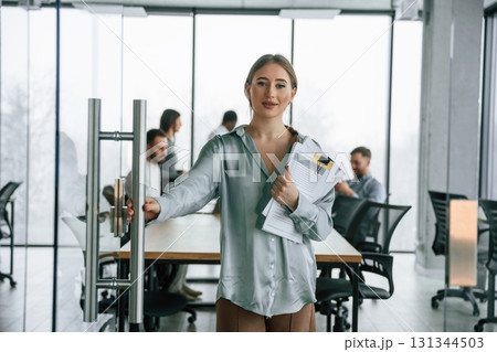 In formal clothes. Woman is standing with documents. Team of office workers are together indoors 131344503