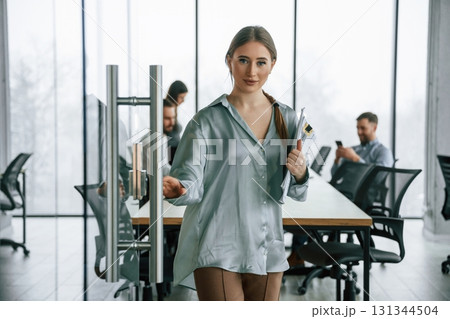 In formal clothes. Woman is standing with documents. Team of office workers are together indoors In formal clothes. Woman is standing with documents. Team of office workers are together indoors 131344504