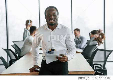 Cheerful man is with documents. Team of office workers are together indoors Cheerful man is with documents. Team of office workers are together indoors 131344550