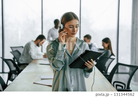 Call center. Woman in headphones. Team of office workers are together indoors Call center. Woman in headphones. Team of office workers are together indoors 131344562