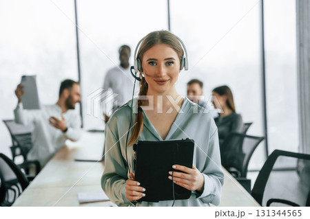 Call center. Woman in headphones. Team of office workers are together indoors Call center. Woman in headphones. Team of office workers are together indoors 131344565