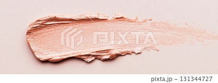 Peach colored cosmetic product is smeared on a light pink surface, creating a textured swatch that showcases its creamy consistency and subtle shimmer 131344727
