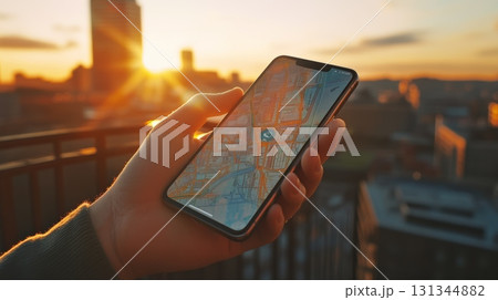 Hand holding smartphone displaying navigation app with map and location marker, overlooking cityscape at sunset from rooftop, providing sense of travel and exploration 131344882