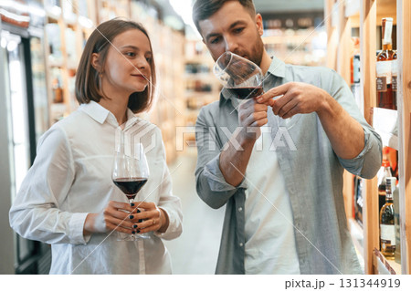 Glasses with drink. Take a sample. Man and woman are choosing wine in the shop 131344919