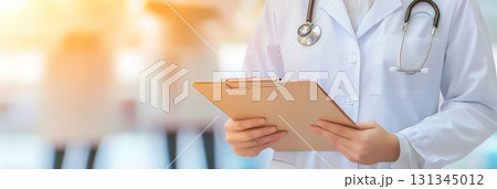 Close up of a female doctor wearing a stethoscope and holding a clipboard, standing in a blurred hospital corridor, conveying professionalism and medical expertise 131345012