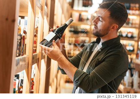 Customer is looking at bottle. Man is choosing wine in the store Customer is looking at bottle. Man is choosing wine in the store 131345119