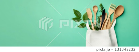 Wooden cutlery set featuring a reusable bag and surrounded by green leaves highlights a commitment to a sustainable lifestyle against a vibrant green background, offering ample copy space 131345232