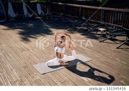 On the yoga mat. Young woman in fitness clothes is outdoors 131345416