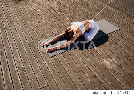 Illuminated by sunlight, practicing yoga. Young woman in fitness clothes is outdoors Illuminated by sunlight, practicing yoga. Young woman in fitness clothes is outdoors 131345444
