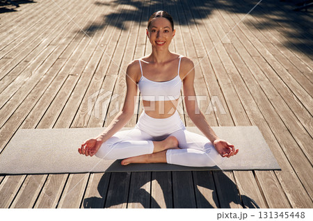 In lotus pose, meditating. Young woman in fitness clothes is outdoors In lotus pose, meditating. Young woman in fitness clothes is outdoors 131345448