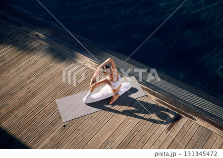 View from the top, doing exercises. Young woman in fitness clothes is outdoors View from the top, doing exercises. Young woman in fitness clothes is outdoors 131345472