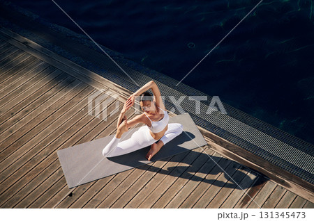 View from the top, doing exercises. Young woman in fitness clothes is outdoors View from the top, doing exercises. Young woman in fitness clothes is outdoors 131345473