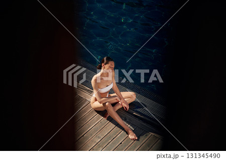 Resting, enjoying the vacation. Woman in white bikini is near swimming pool 131345490