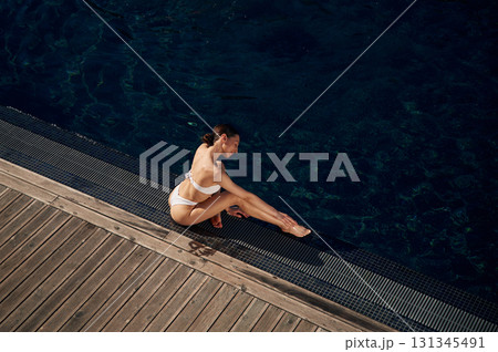 Resting, enjoying the vacation. Woman in white bikini is near swimming pool Resting, enjoying the vacation. Woman in white bikini is near swimming pool 131345491