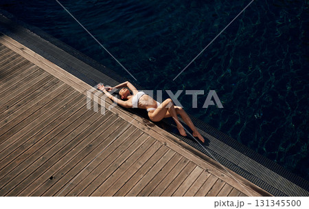 Wooden floor, lying down, resting. Woman in white bikini is near swimming pool Wooden floor, lying down, resting. Woman in white bikini is near swimming pool 131345500