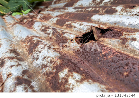 Close-up of rusty corrugated metal sheet with a hole, corrosion texture and decay detail Close-up of rusty corrugated metal sheet with a hole, corrosion texture and decay detail 131345544