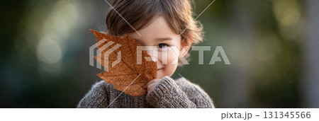 Portrait of a cheerful child holding a large dry leaf in front of their face, partially obscuring it, in a playful gesture during a sunny autumn day outdoors, with a blurred natural background Portrait of a cheerful child holding a large dry leaf in front of their face, partially obscuring it, in a playful gesture during a sunny autumn day outdoors, with a blurred natural background 131345566