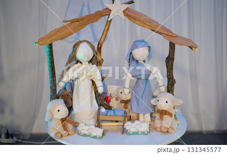 A whimsical, handcrafted Nativity scene featuring stylized rag dolls representing Mary and Joseph, along with plush sheep and a wooden manger. A whimsical, handcrafted Nativity scene featuring stylized rag dolls representing Mary and Joseph, along with plush sheep and a wooden manger. 131345577